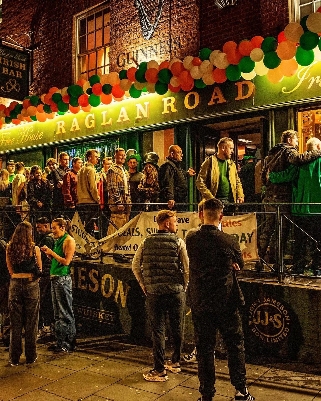 Guests queueing outside Raglan Road on Derby Road under green, white and orange balloons